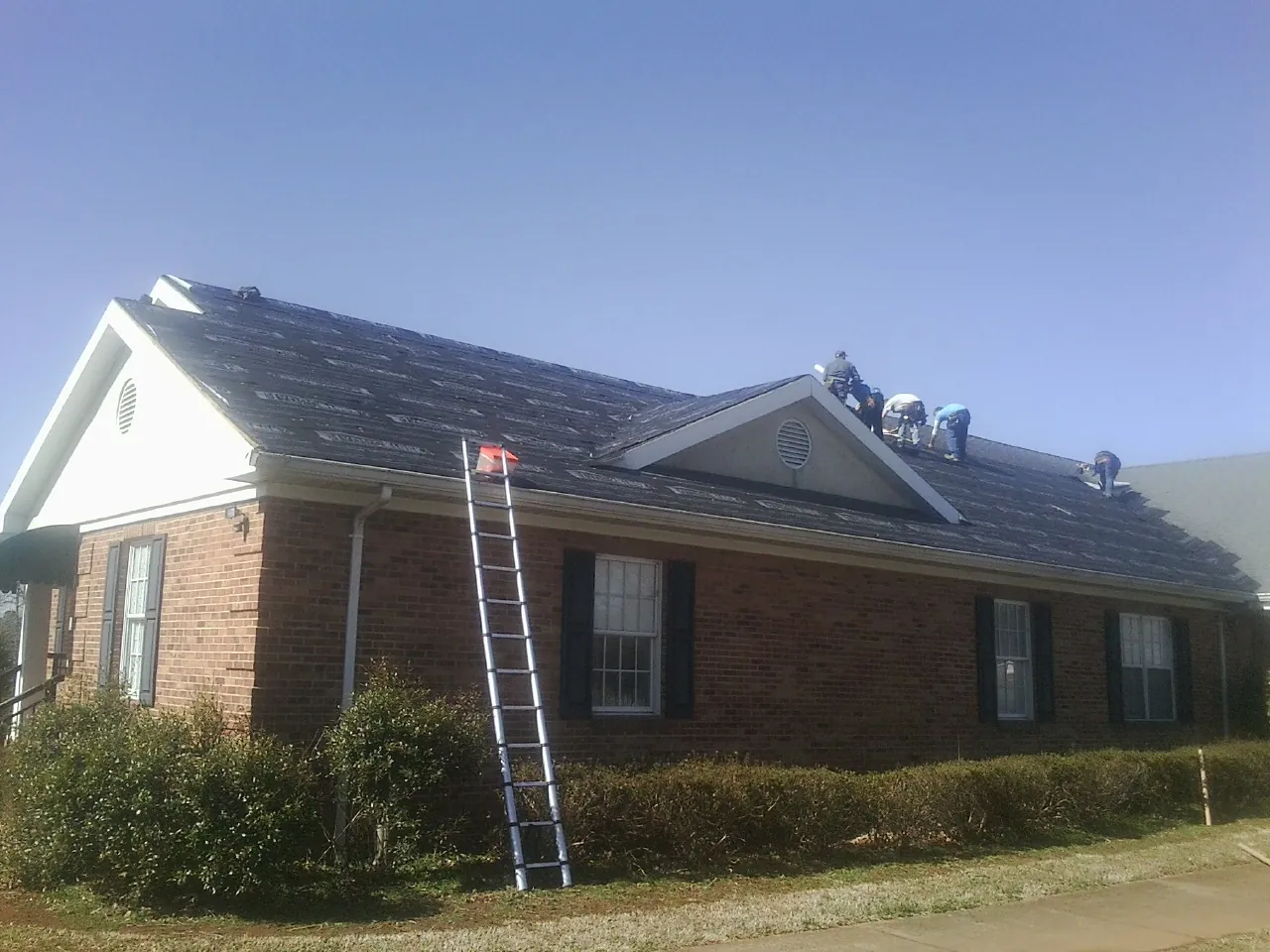 Crew tearing shingles off a brick ranch roof with a ladder set — Emergency Roof Repair work by our crew in Loami