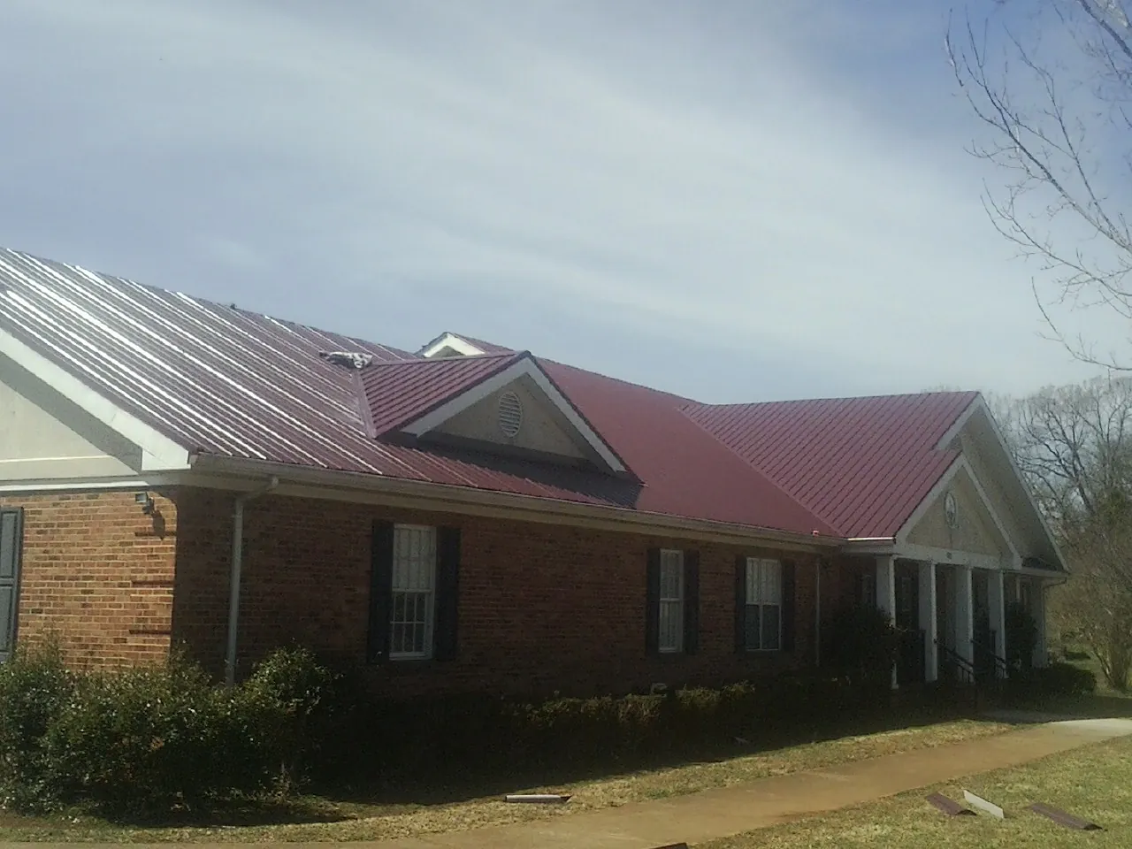 Red metal roof with gabled entries on a long brick building, from a Hail Damage Roof Repair job in Loami