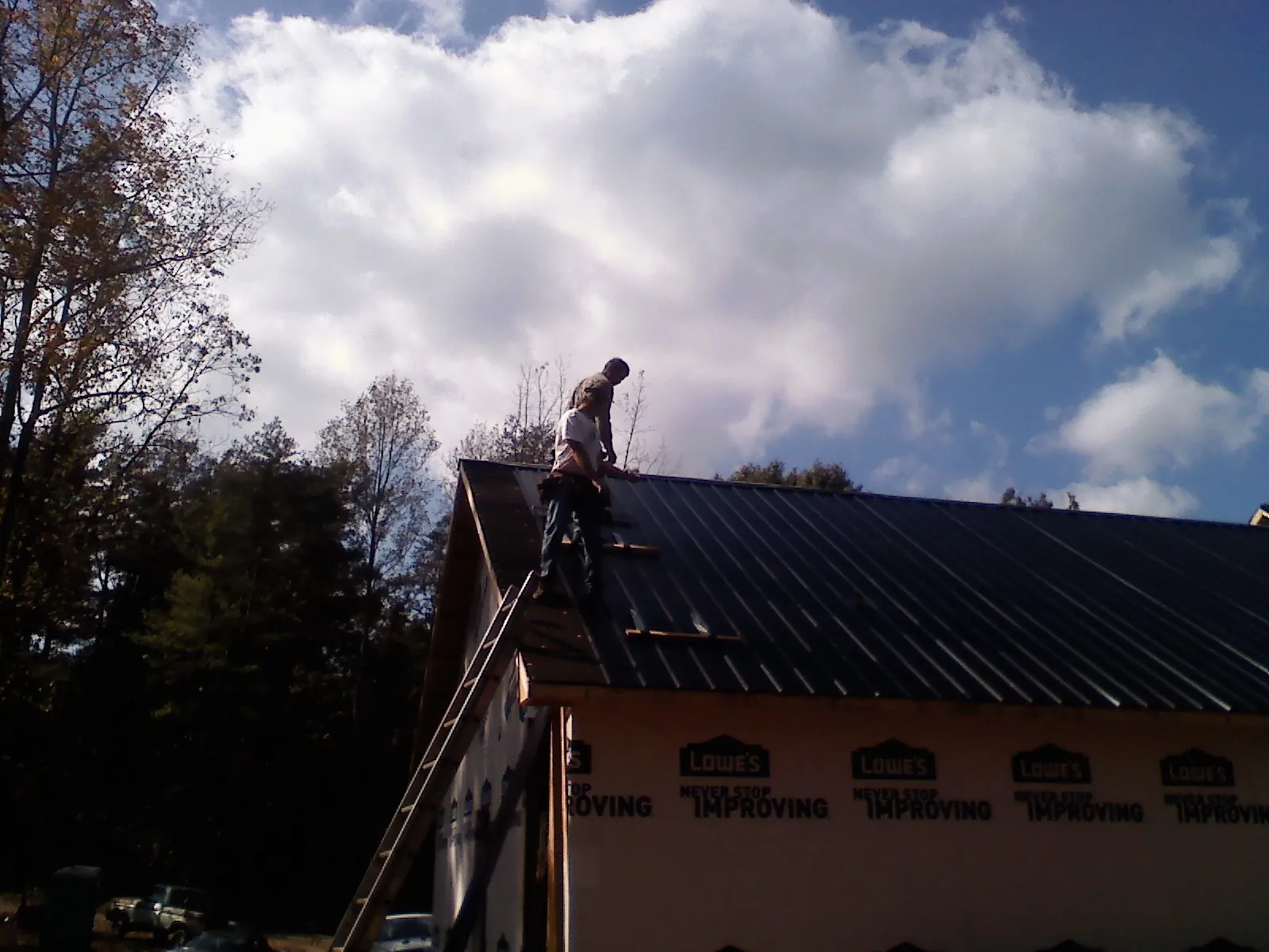 Roofer fastening dark metal panels high against a cloudy sky, from a Roof Inspection job in Loami